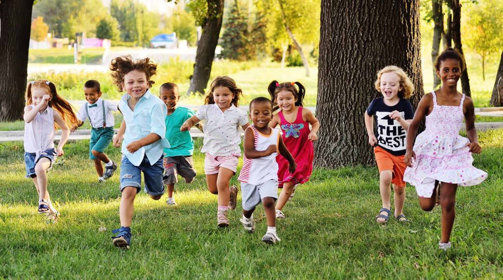 Multi-ethnic group of young children kids running on the grass in the park, photo